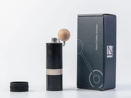 Black IZpresso Q Air hand coffee grinder with wooden top next to its packaging on a white background