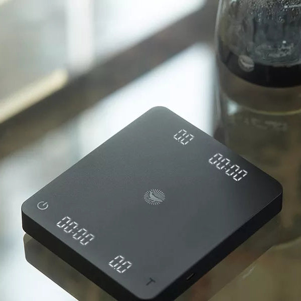 Black digital kitchen scale on a glass surface with a blurred background