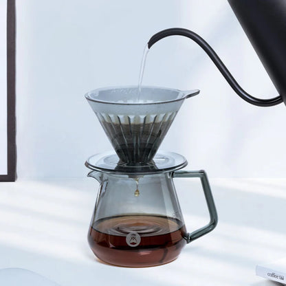 Coffee being poured from a kettle into a glass carafe with a filter.