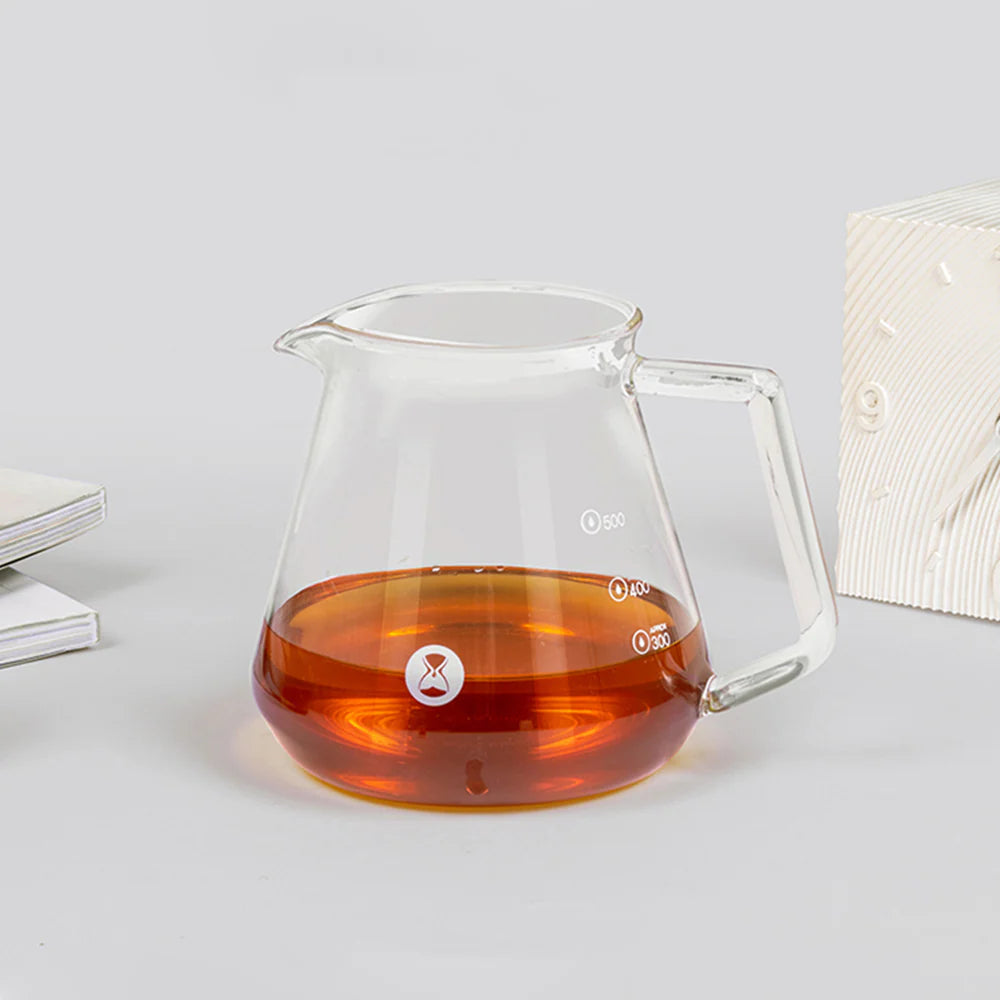 Clear glass coffee server with amber liquid on a light gray background