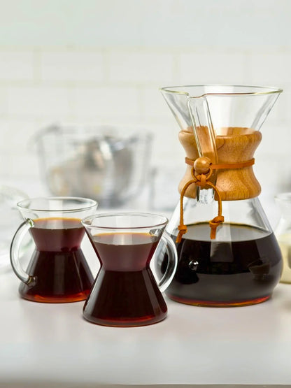 Chemex coffee maker with two glasses of coffee on a white surface