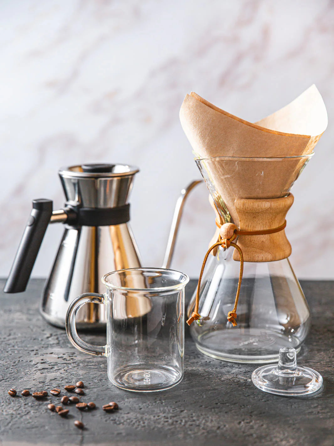 Coffee-making setup with a pour-over coffee maker, glass mug, and coffee beans on a dark surface.