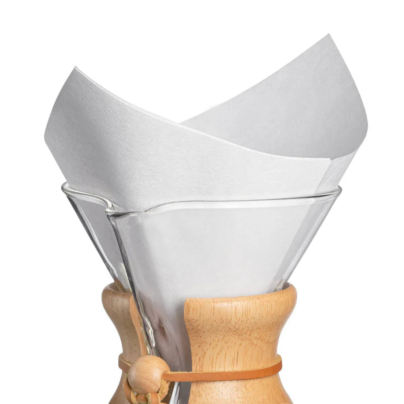 Clear glass coffee maker with wooden collar and white paper filter on a white background