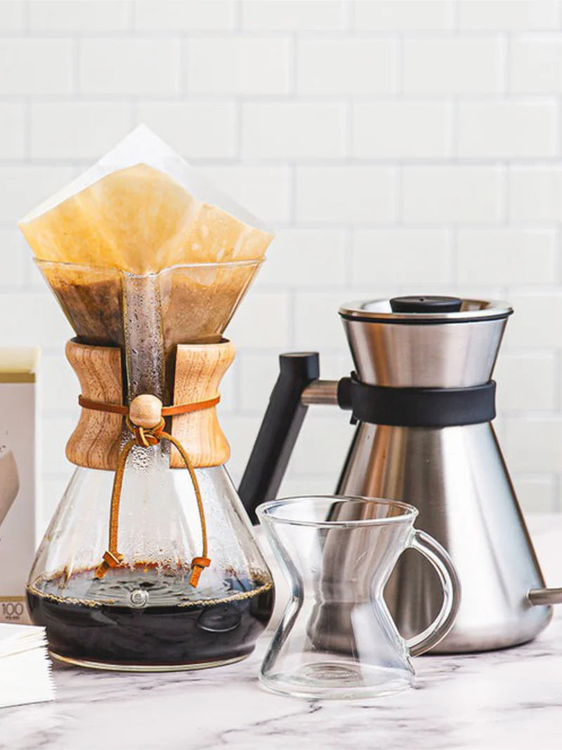 Coffee brewing setup with a Chemex and a stainless steel pour-over coffee maker on a marble surface.