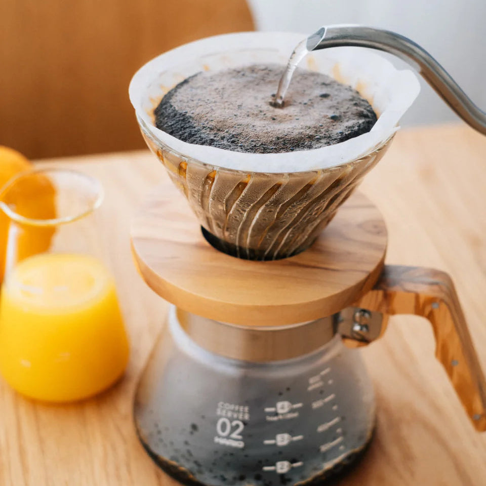 Coffee brewing process with a filter and wooden collar on a wooden table.