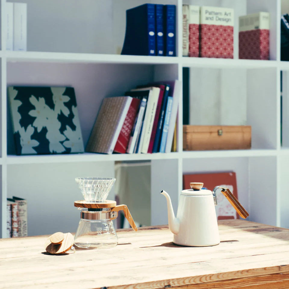 White kettle on a wooden table with a bookshelf in the background