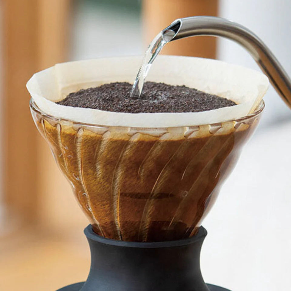 Coffee brewing process with water being poured over coffee grounds in a glass filter.