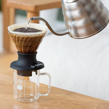 Coffee brewing process with a kettle pouring water into a coffee filter on a wooden table.